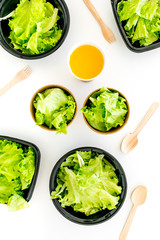 Healthy fast food concept. Light meal with lettuce in plastic containers near wooden spoons and green tea on white background top view