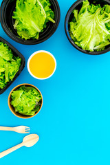 Food delivery concept. Healthy food. Diet meal with lettuce in plastic boxes, green tea, disposable tableware on blue background top view copy space