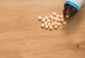 Open bottle with pills on wooden background.