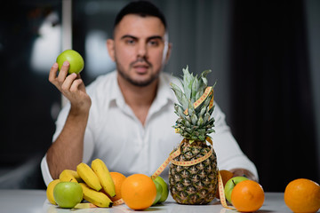 Attractive man with an apple in his hand sitting at a table on which lie fresh fruit. The concept of a healthy lifestyle