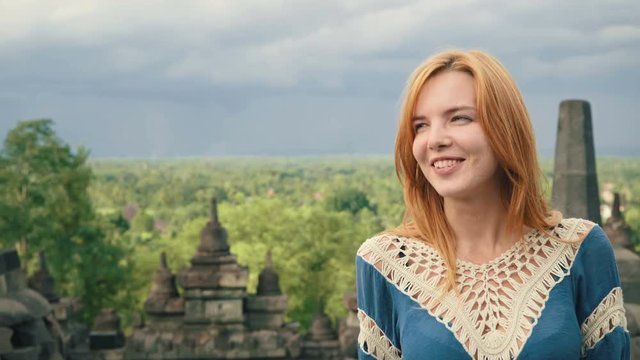 Close up of young caucasian happy woman on top of Borobudur temple in front of stone stupas and view to forest in Java, Indonesia