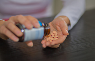 Woman hands holding bottle of pills in one hand and pile of tablets on other hand.