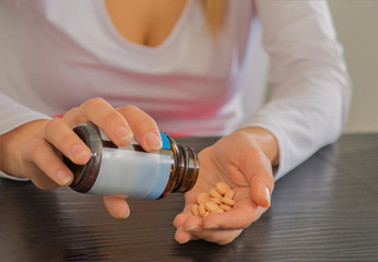 Woman hands holding bottle of pills in one hand and pile of tablets on other hand.