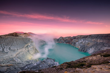 Active crater volcano with smoke of sulphur in turquoise lake with colorful sky at morning