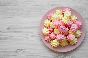 Mini meringues on pink plate on a white wooden background, top view. Close-up. Copy space.