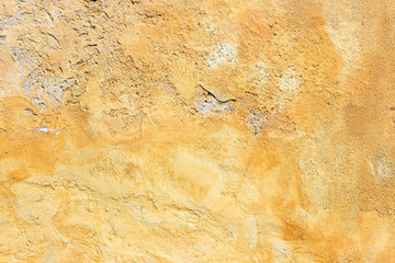 Old yellow painted uneven plaster concrete wall fragment detail background