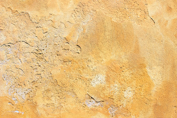 Old yellow painted uneven plaster concrete wall fragment detail background