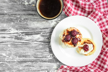 Cottage cheese pancakes with strawberry jam on white plate on grey wooden background. Healthy breakfast.