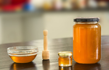 Small and big jar of honey with small bowl on kitchen background.