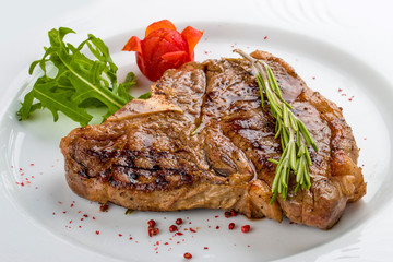 Steak T-bone with greens. On a white plate.