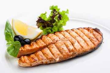 Salmon steak with lemon on a white plate.