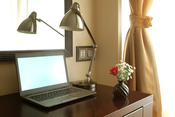 Laptop notebook computer on wood dark brown working desk with modern lamp and little vase of flowers closed to window and curtain