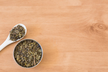 Dry green tea leaves on bowl and ceramic spoon.