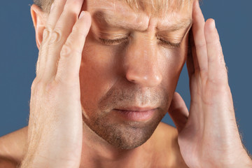 A man holds his hands on his head on blue background. Headache or migraine.