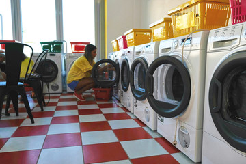 The girl in the self-service Laundry loads Laundry into the washing machine. Room with laundry machines. Sunny summer day. No people.