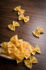Pasta in the form of a butterfly in a wooden bowl on a wooden background near the ears of wheat. wooden spoon with pasta in the form of a butterfly
