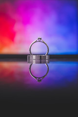 Close up of beautiful titanium ring given by groom to the bride on wedding day. Isolated on colorful background with reflection on glass surface.