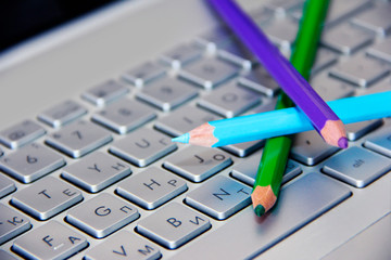 blue green and purple pencils lie on a silver computer keyboard