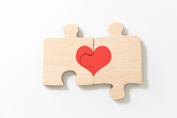 Two joined pieces of wooden puzzle, with red heart, on white background.