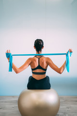 Young sporty attractive woman practicing pilates with resistance bands back sitting on fitness balls on white urban studio. Yoga and Pilates lifestyle healthy concept. - obrazy, fototapety, plakaty