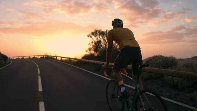 A young sports man riding a bike on a mountain serpentine in a yellow t-shirt helmet and sports equipment rear view . Slow motion steadicam