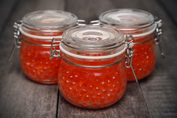Red caviar in glass jars on a rustic wooden table. Sea organic food. Healthy diet eating.