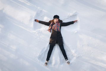 A young caucasian girl on the snow shows an angel. Spreading arms. Top view. Drone. Smile. Happy.