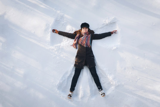 A young caucasian girl on the snow shows an angel. Spreading arms. Top view. Drone. Smile. Happy.