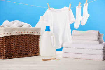 plastic containers with laundry liquids, laundry basket, pile of towels and clean white clothes on blue