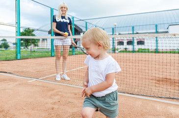 Beautiful blonde-haired mother with her little daughter playing on the tennis court.