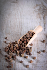Pepper peas in a wooden spoon on a wooden background. Spices are scattered on the table