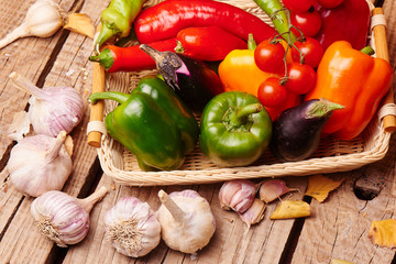 Cherry tomatoes, peppers, garlic, eggplants in a wicker basket. Fresh vegetables on a wooden table..