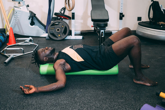 Black attractive strong man Doing an Exercise with Foam Roller on his Upper Back in a gym. Sport.