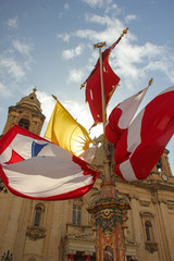 Waving red, yellow and white flags on festively decorated square near old church for annual festa...