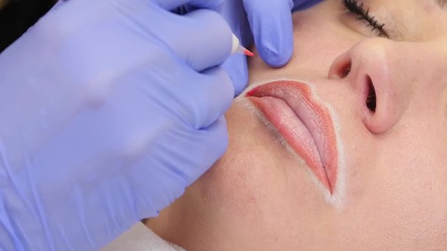 Young woman having permanent makeup on lips in beautician salon. slow motion