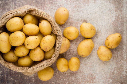 Sack of fresh raw potatoes on wooden background, top view.