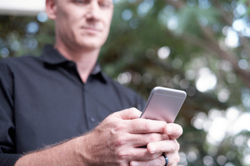 Low angle close-up view of defocused middle-aged Caucasian man texting on modern smartphone outdoors