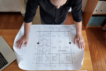High angle view of unrecognizable mature man looking at large blueprint of ceiling while standing...