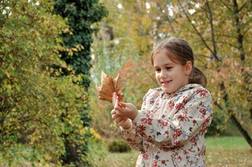 Caucasian 8-9 years old child, girl, happy in the park, playing with dried autumn leaves