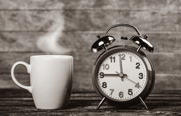 Cup of coffee and alarm clock on wooden table. Image in black and white color style