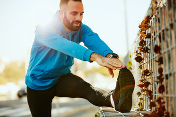 Young bearded male runner stretching legs before running. Wearing sportswear, healthy lifestyle...