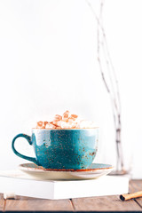 Hot chocolate with marshmallows and cinnamon stick in a blue ceramic cup on a table with a book. The concept of winter or fall time. Minimal scandinavian design.