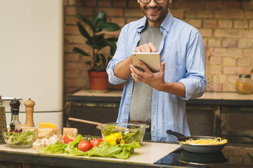 Man preparing delicious and healthy food in the home kitchen on a sunny day. Using tablet computer...