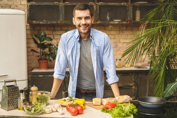 Portrait of young man preparing delicious and healthy food in the home kitchen on a sunny day. Smiling and looking at camera.