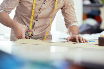 Close-up of tailor working with cloth at table, he cutting textile with scissors at atelier