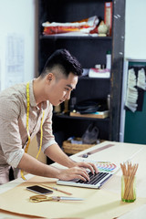 Young fashion designer sitting at the table and typing at laptop