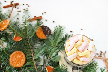 holidays, winter and celebration concept - hot chocolate drink with marshmallows, cinnamon, dry oranges, coffee beans and fir tree on white background. Winter christmas holiday background. Flat lay