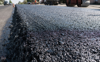Freshly laid black bitumen asphalt with a high edge to the gravel showing the structure. Laying a...