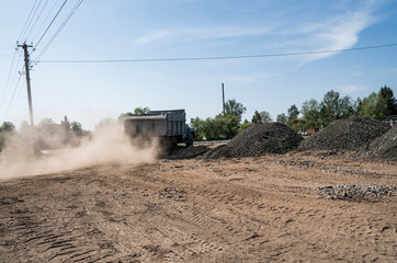 A truck with stones in the trailer moves along the way, picking up a dust.