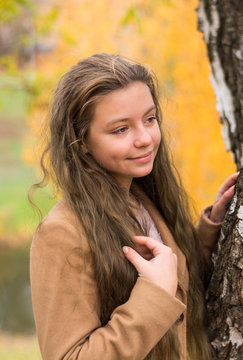Girl-teenager in a coat stands in the autumn park at a yellow foliage background.